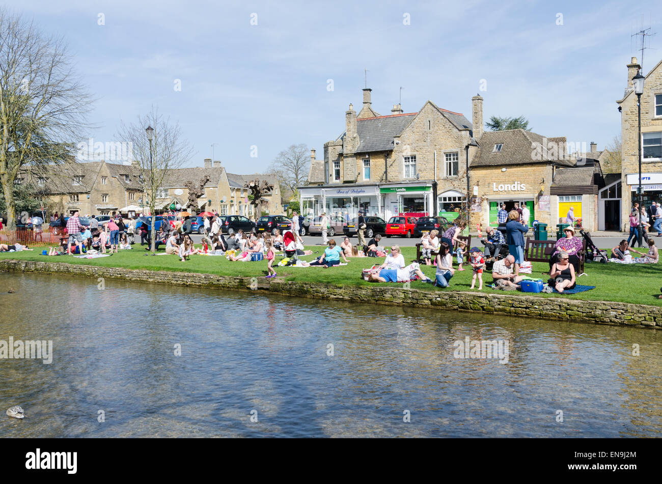 I visitatori godere picnic a lato del flusso in esecuzione attraverso Bourton sull'acqua in Cotswolds Foto Stock