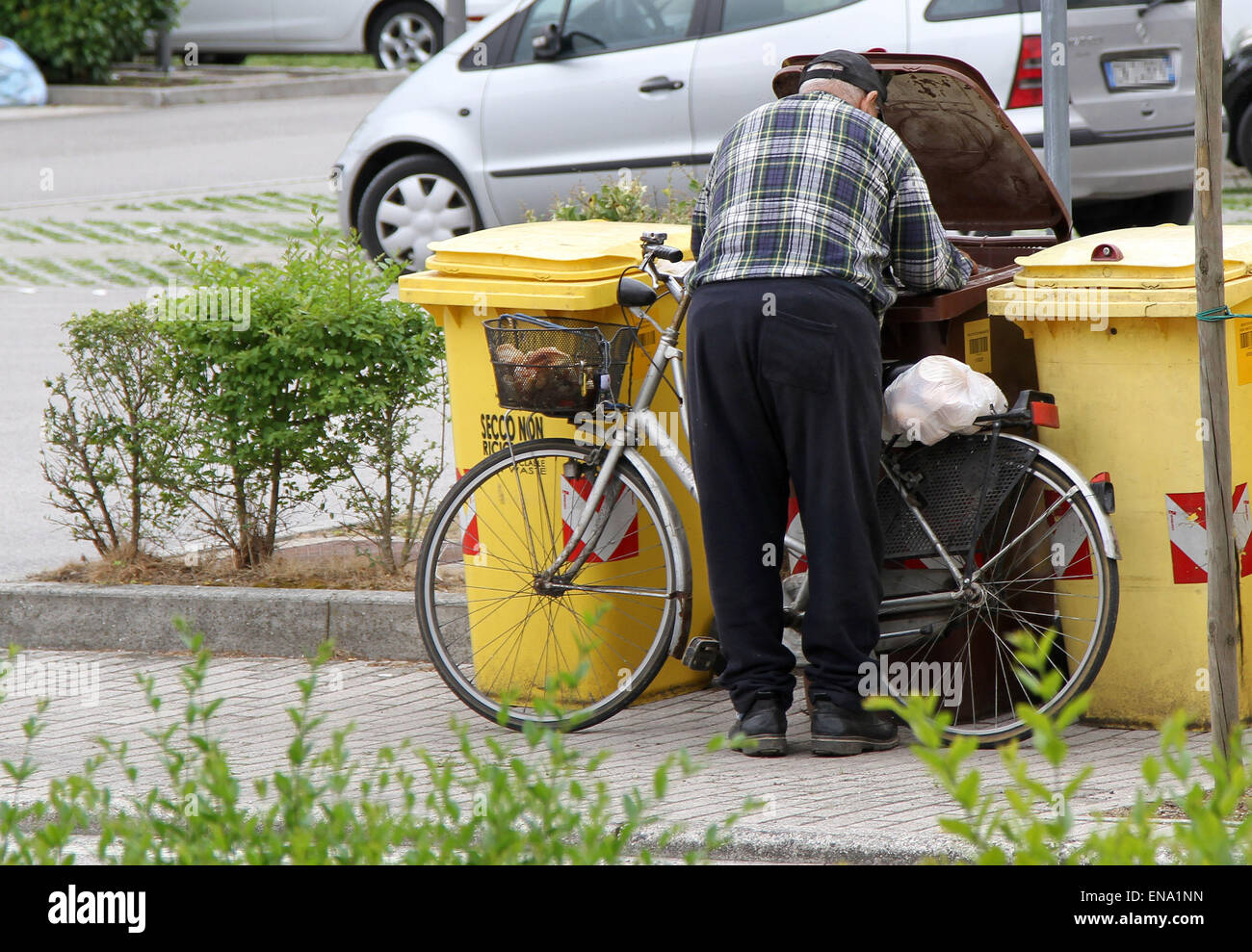 L'Italia, Pordenone: un vecchio uomo cerca nella spazzatura per andare a mangiare qualcosa, mentre a Milano è iniziato Expo 2015 Foto Stock