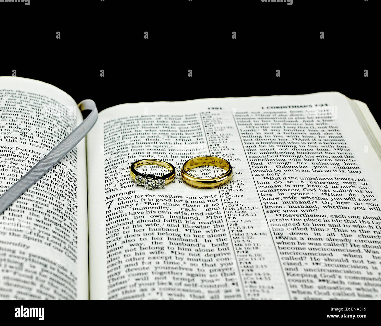 Aprire la Bibbia con il fuoco selettivo sul matrimonio passaggio con due oro gli anelli di nozze su sfondo nero Foto Stock