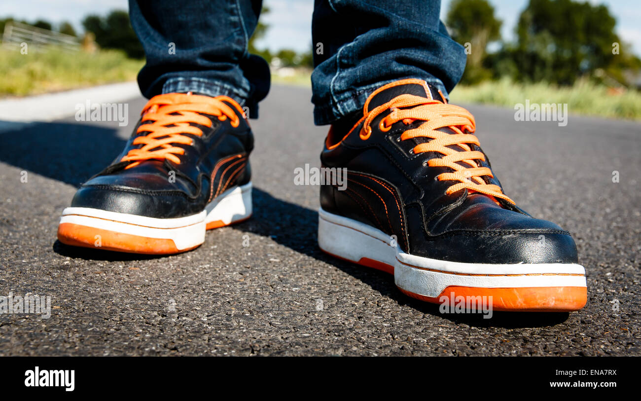 Una persona che cammina su orange nero scarpe sportive su una strada asfaltata. Foto Stock