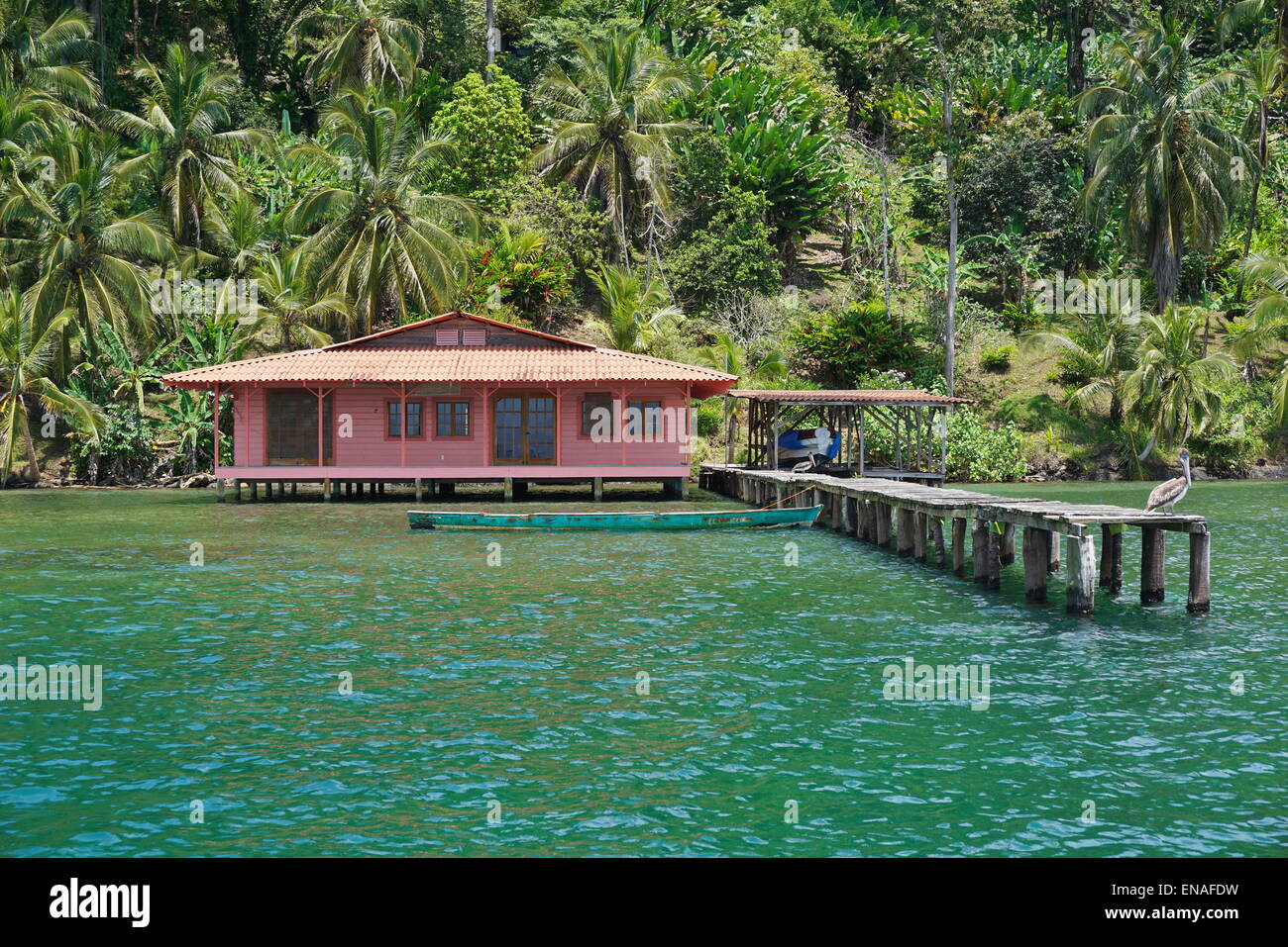 Tropical home sul mare con pelican sul suo dock e la lussureggiante vegetazione sulla costa dei Caraibi, Bocas del Toro, Panama, centrale Foto Stock