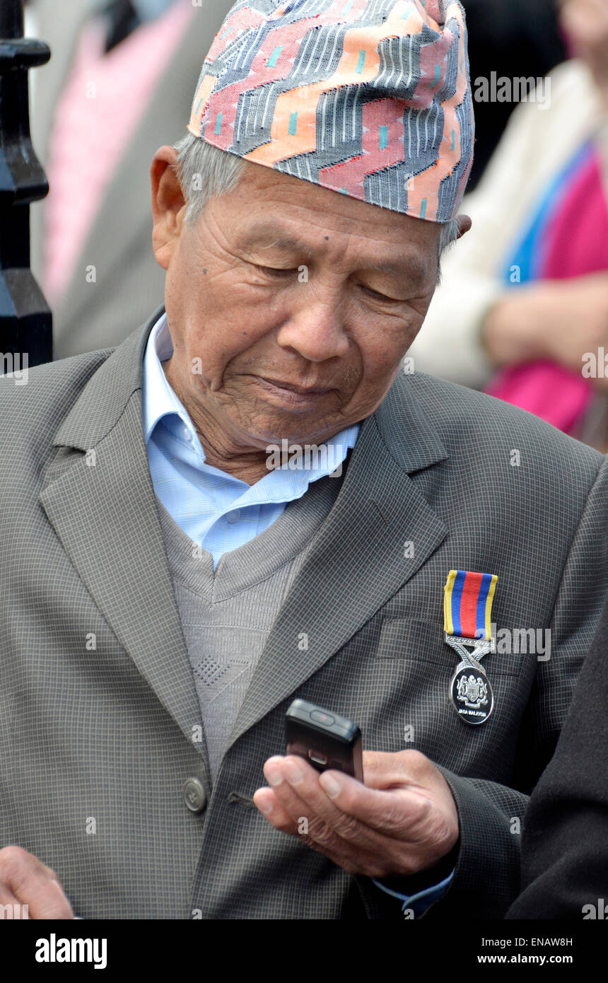 Anziani uomo Nepalese / pensionati Gurkha utilizzando il suo telefono cellulare, Londra 2015, indossando un Dhaka topi - tradizionale hat Foto Stock