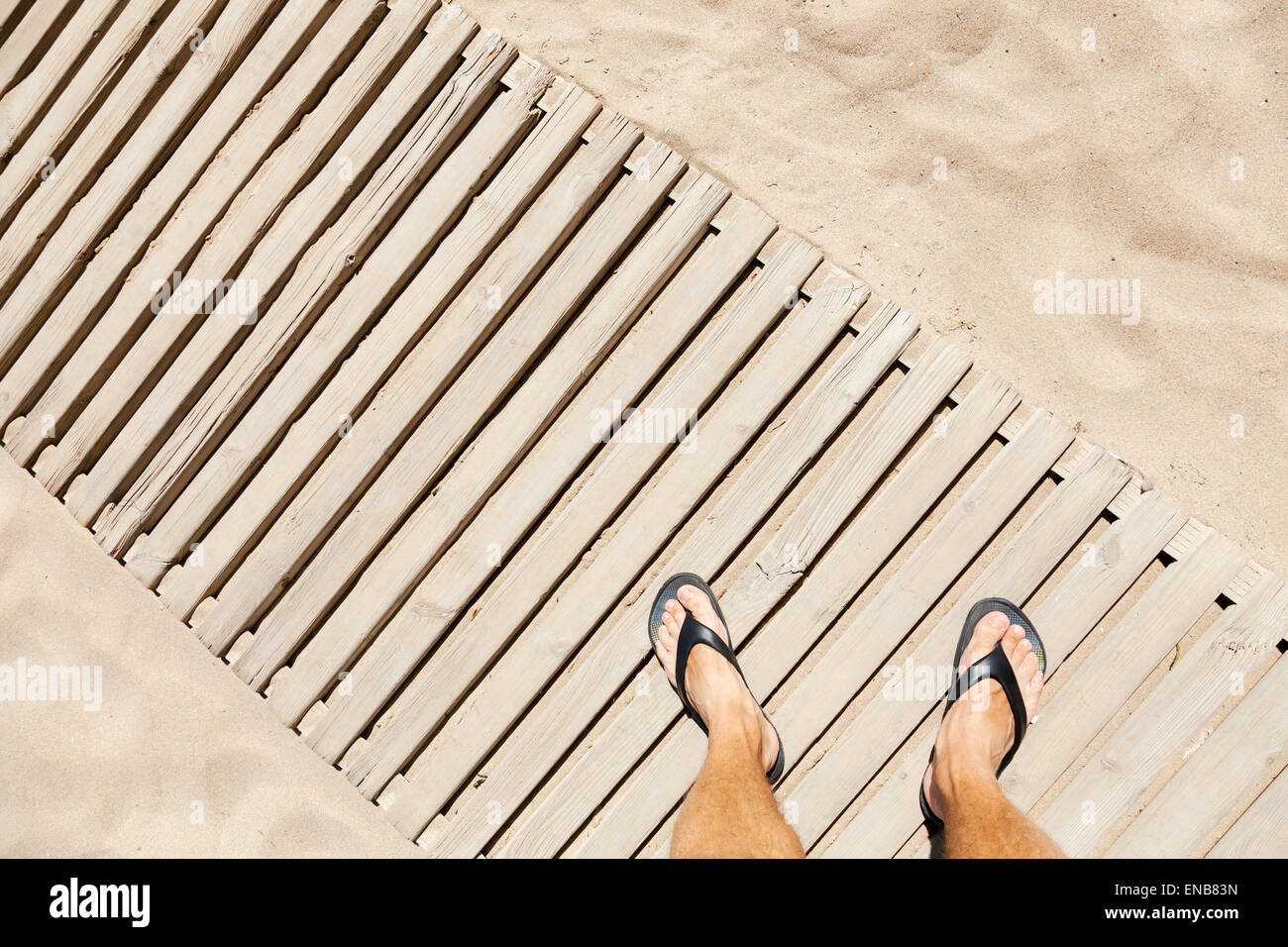 Le gambe del giovane uomo caucasico permanente sulla passerella di legno su una spiaggia di sabbia Foto Stock