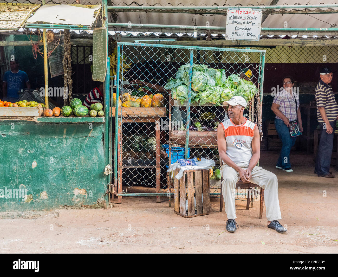 Un uomo afro-cubane si trova appena al di fuori di un mercato pubblico con le verdure sul display dietro di lui a l'Avana, Cuba. Foto Stock