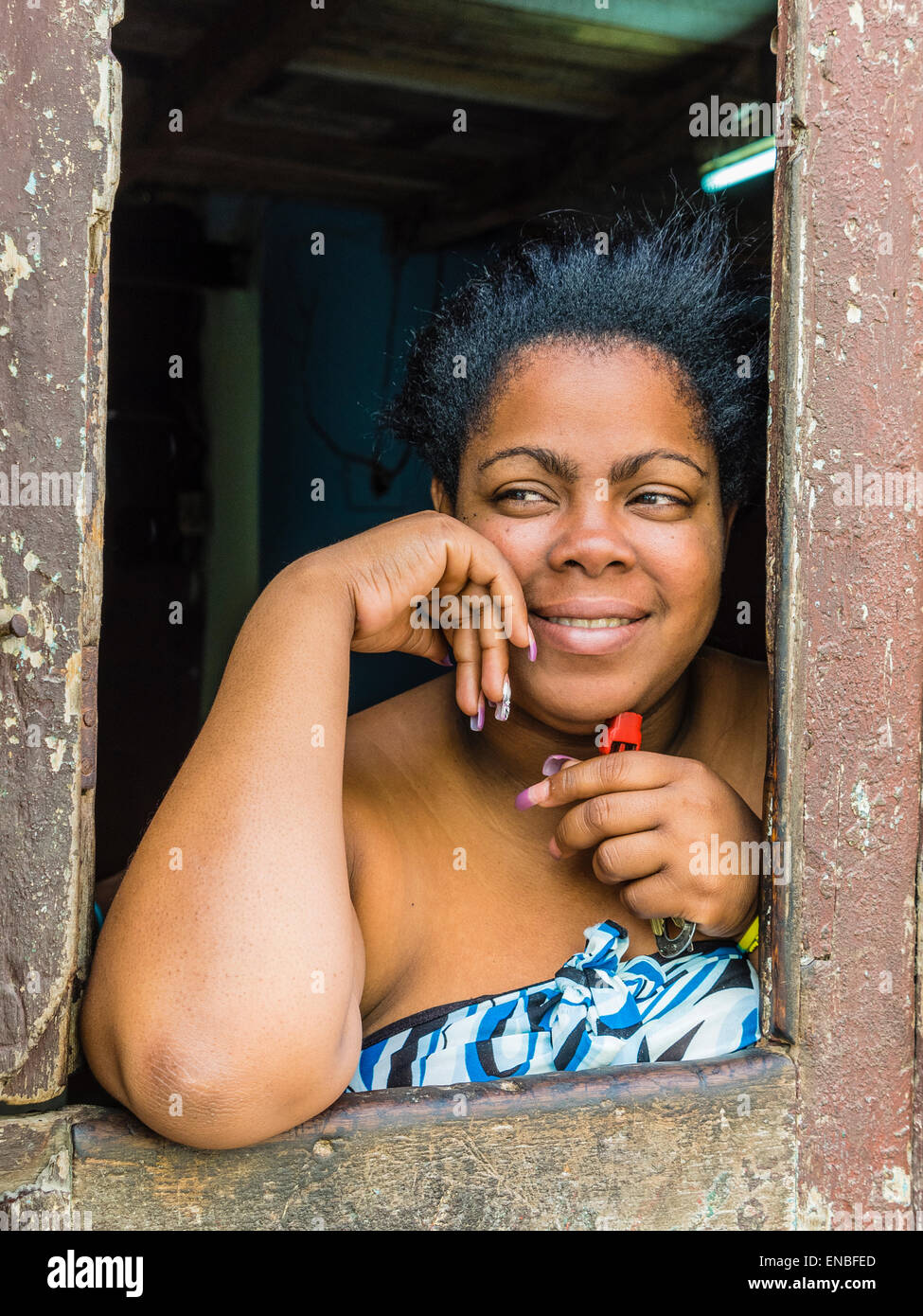 Una donna afro-cubane si appoggia sulla battuta di una porta di apertura e si affaccia verso la strada a l'Avana. Foto Stock
