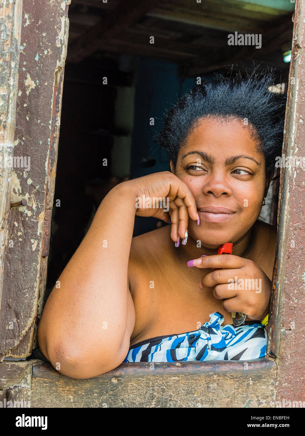 Una donna afro-cubane si appoggia sulla battuta di una porta di apertura e si affaccia verso la strada a l'Avana. Foto Stock