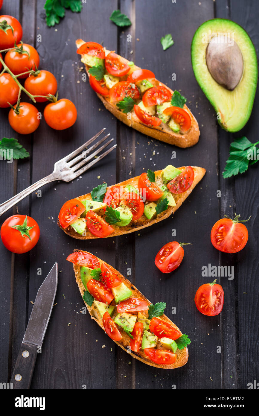 Bruschetta con pomodoro, avocado e erbe su un tavoli in legno nero Foto Stock