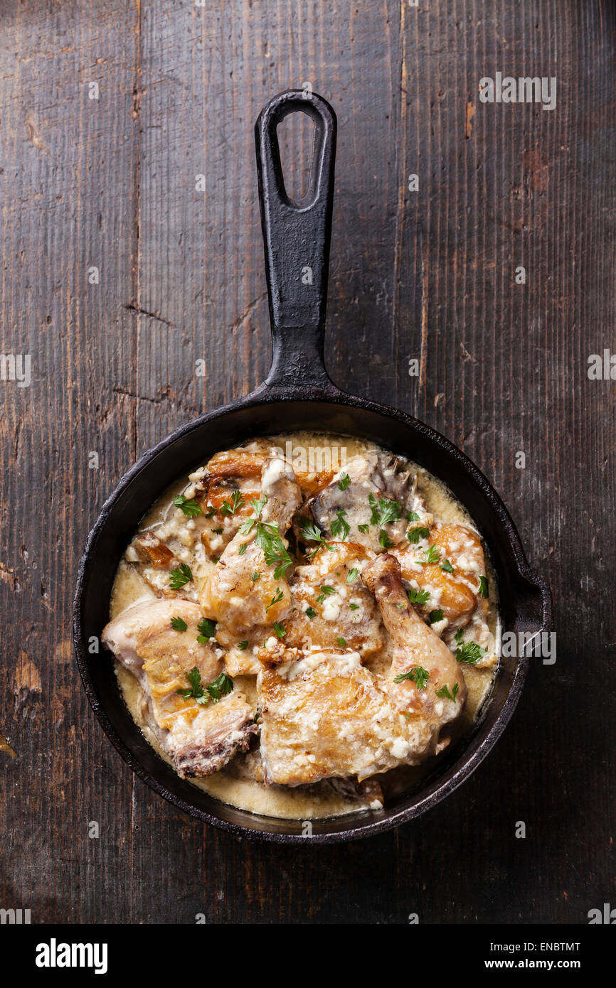 Pollo arrosto con cremosa salsa di aglio in ghisa padella scuro su sfondo di legno Foto Stock