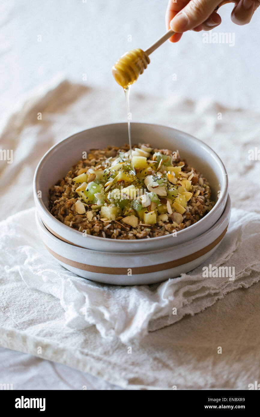 Almond-Kasha porridge con zenzero e ananas collocato in una ciotola e il miele viene spruzzata su di esso. Foto Stock