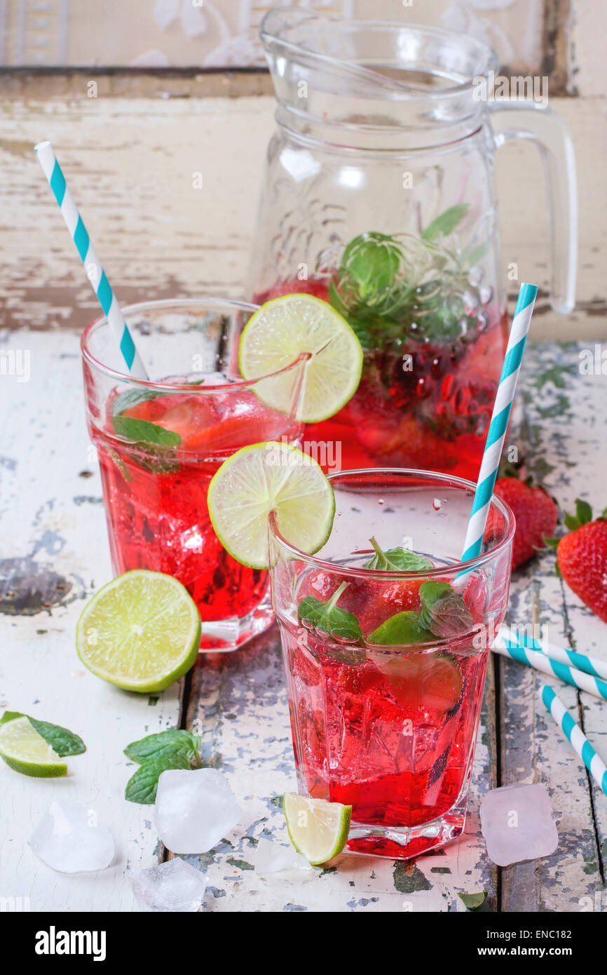 Due bicchieri con cocktail retrò tubi e caraffa di vetro di fragole fatta in casa la limonata, servita con fragole fresche, menta, calce Foto Stock