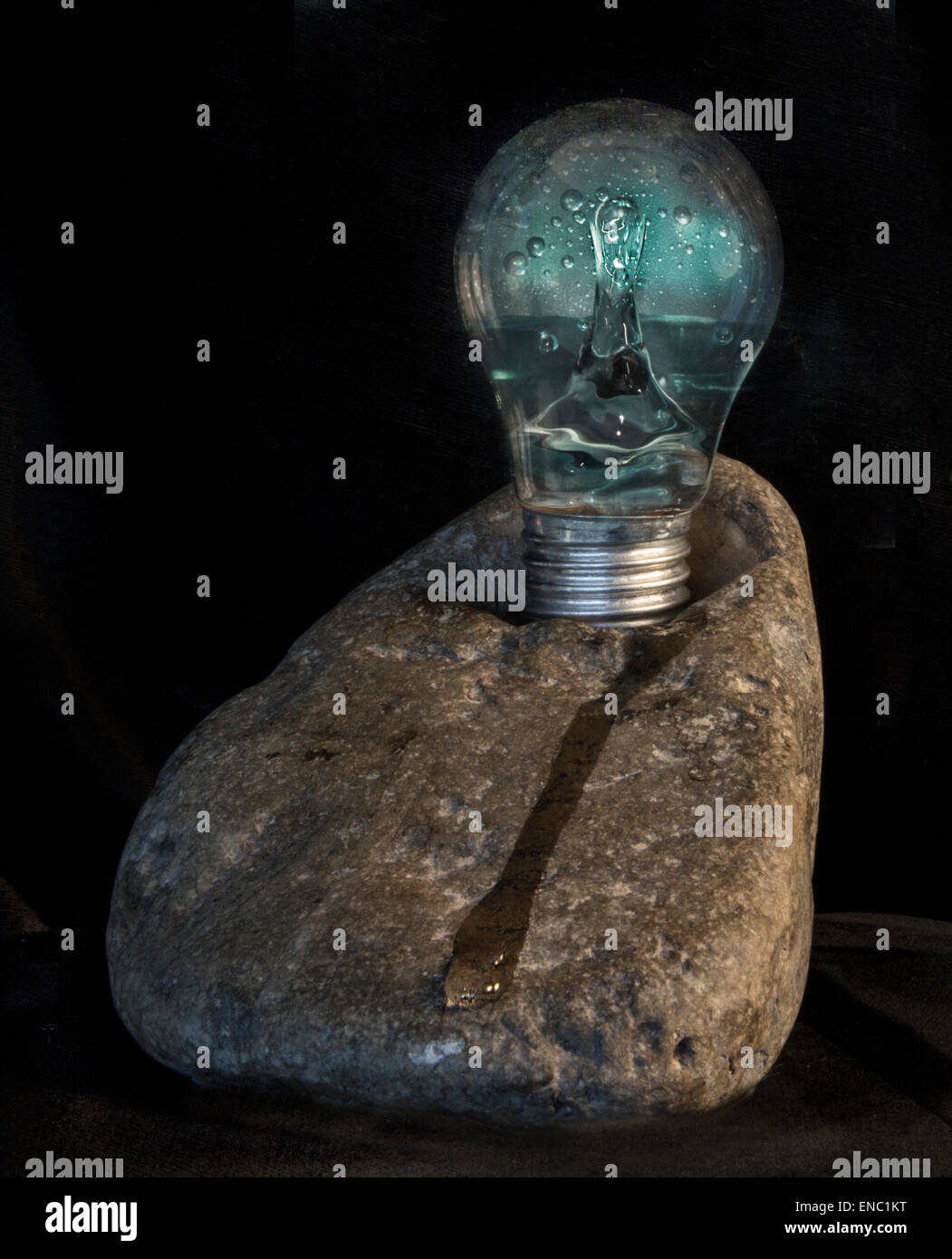 Una immagine creativa di energia idroelettrica rappresentato da uno spruzzo di acqua in una lampadina posta su di una roccia Foto Stock
