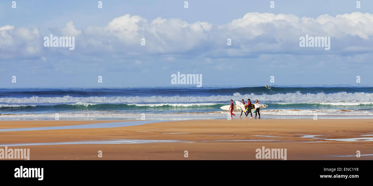 Gruppo di amici surfisti in Costa de Caparica beach. Pioneer iconico punto surf in Portogallo e camminando per trasportare le tavole da surf felice con la tavola da surf onde del mare Foto Stock