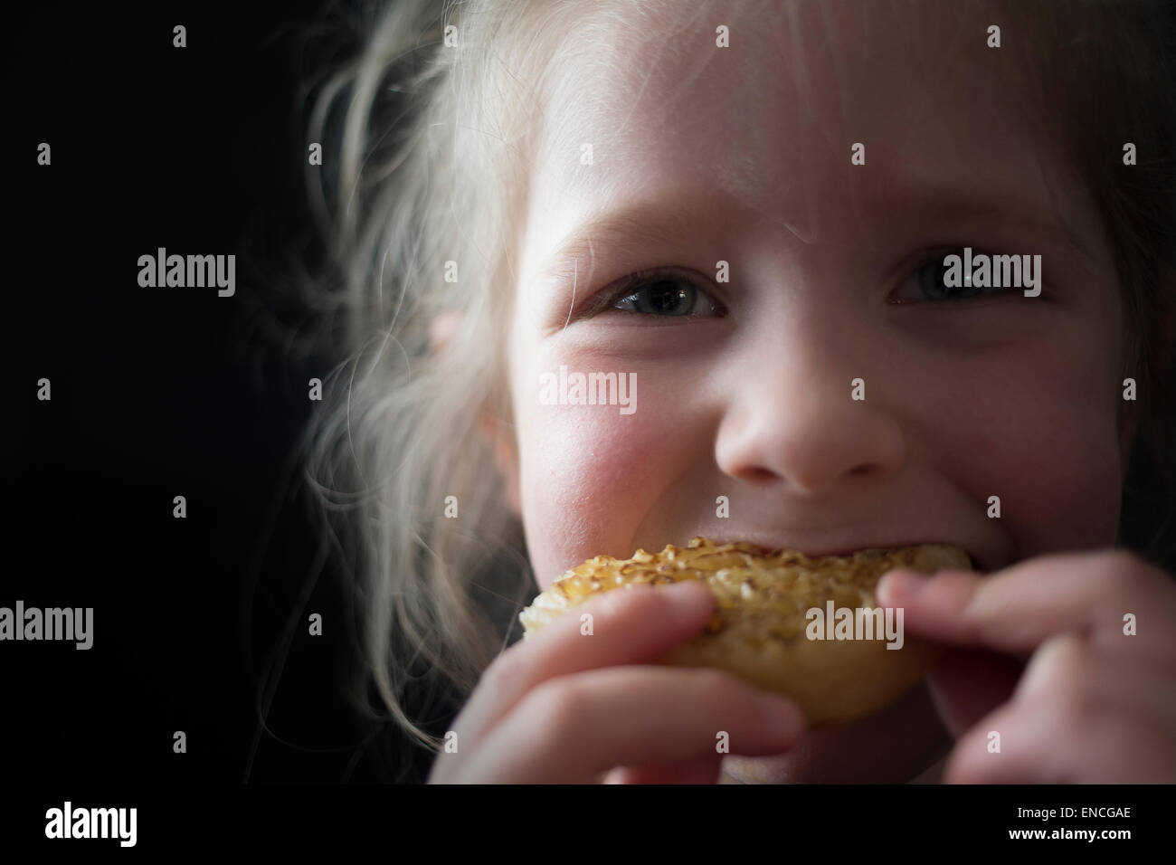 Cinque anni di giovane ragazza di mangiare un crumpet su uno sfondo nero. Di fronte alla fotocamera. Foto Stock