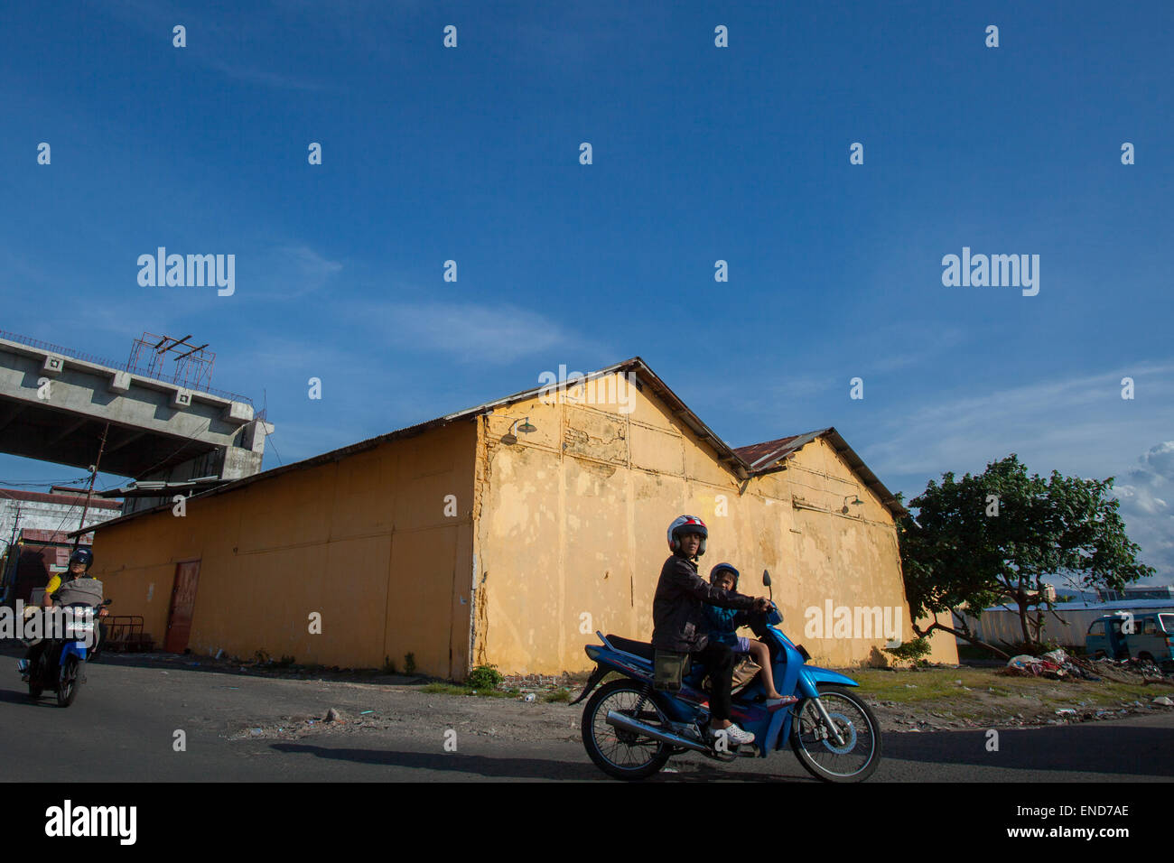 Gli automobilisti sono fotografati sullo sfondo di un edificio di magazzino, nella zona costiera di Manado, Sulawesi settentrionale, Indonesia. Foto Stock