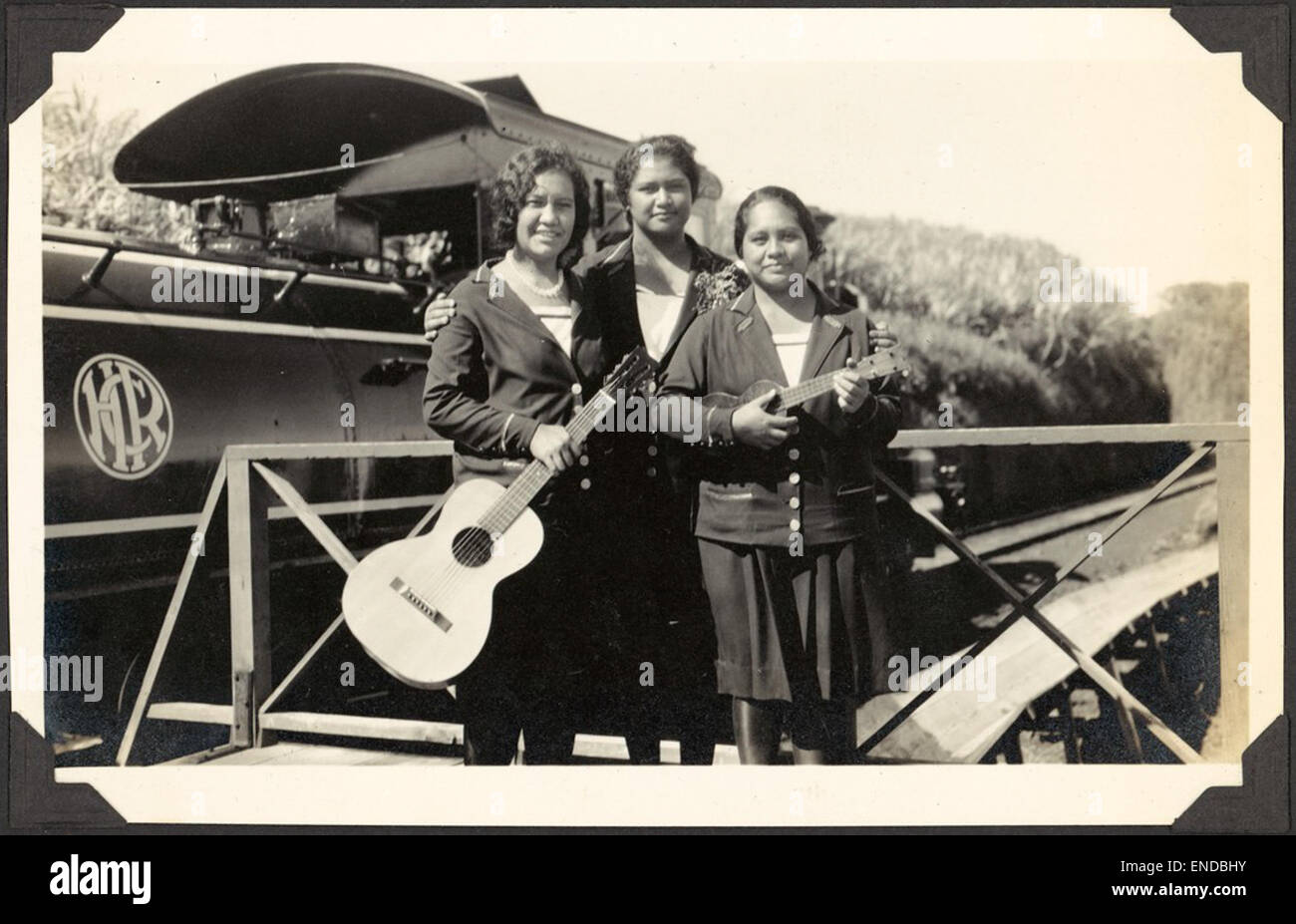 Tre giovani donne con una chitarra e un ukelele, sostare davanti a un Hawaii consolidato steamtrain ferroviaria, Regione di Hilo, Hawaii, 1929 / C.M. Yonge tre giovani donne con una chitarra e un ukelele, stand Foto Stock