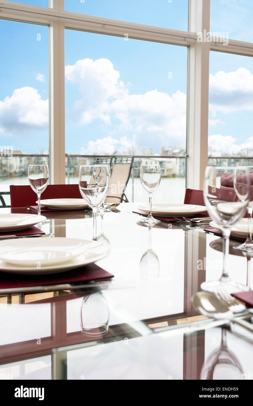 Un vetro tavolo da pranzo insieme con le regolazioni del posto, bicchieri da vino & Piastre per un pasto di festa Foto Stock