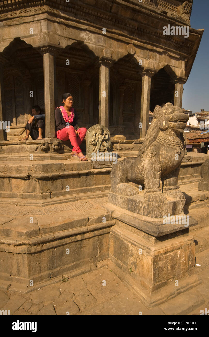 Il Nepal, Kathmandu, Patan Durbar Square, Krishna Mandir Hindu Temple (1637), donna adoratore con lion custode statua di pietra Foto Stock