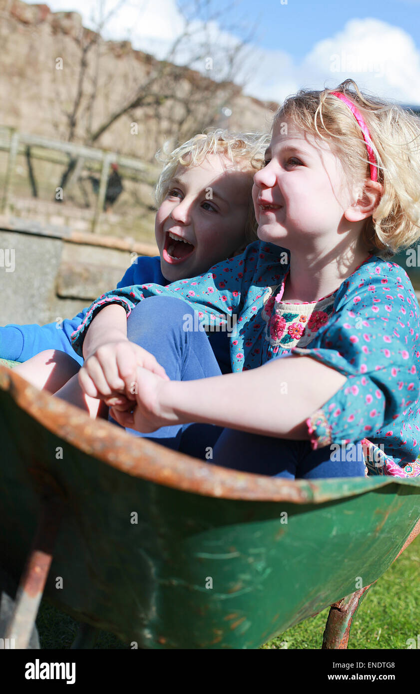 Fratello e Sorella di seduta in una ruota di barrow divertendosi Foto Stock