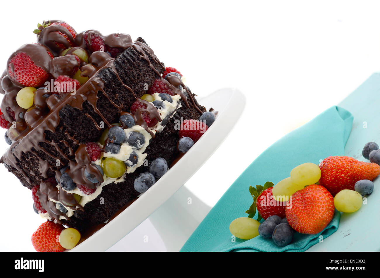 Deliziosamente divina torta al cioccolato con fragole, mirtilli e lamponi e uva e crema su blu pallido shabby chic tab Foto Stock