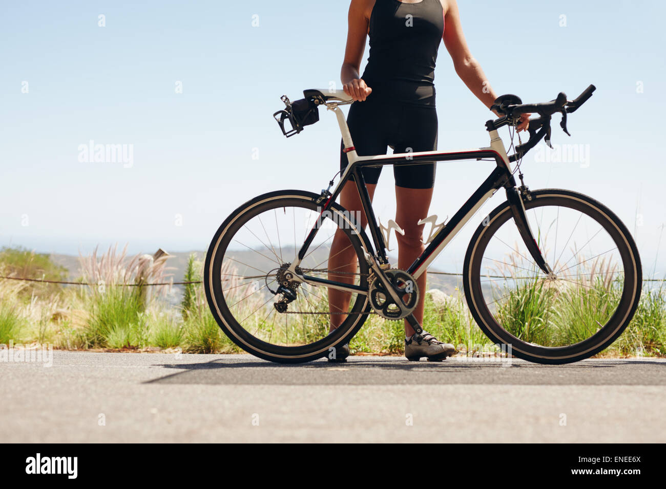 Sezione bassa colpo di atleta femminile in piedi con la sua bicicletta. Donna ciclista con la sua bici su strada di campagna. Ritagliato colpo di femal Foto Stock