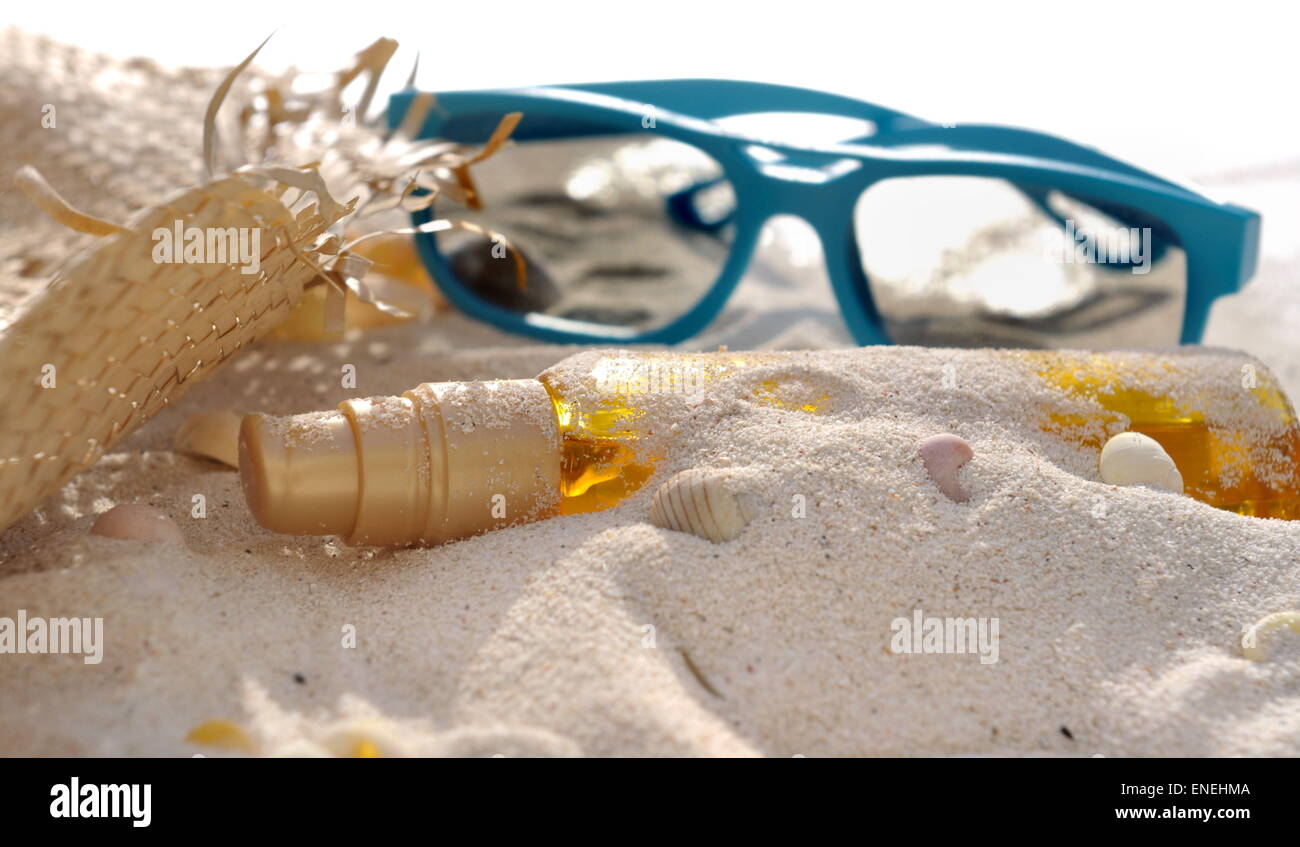 Bottiglia di olio abbronzatura coperto di sabbia con cappello e occhiali da sole Foto Stock