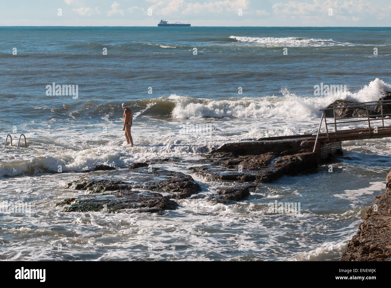 L'uomo anziano con swim cap si prepara a nuotare in mare mosso, nave da carico in background Foto Stock