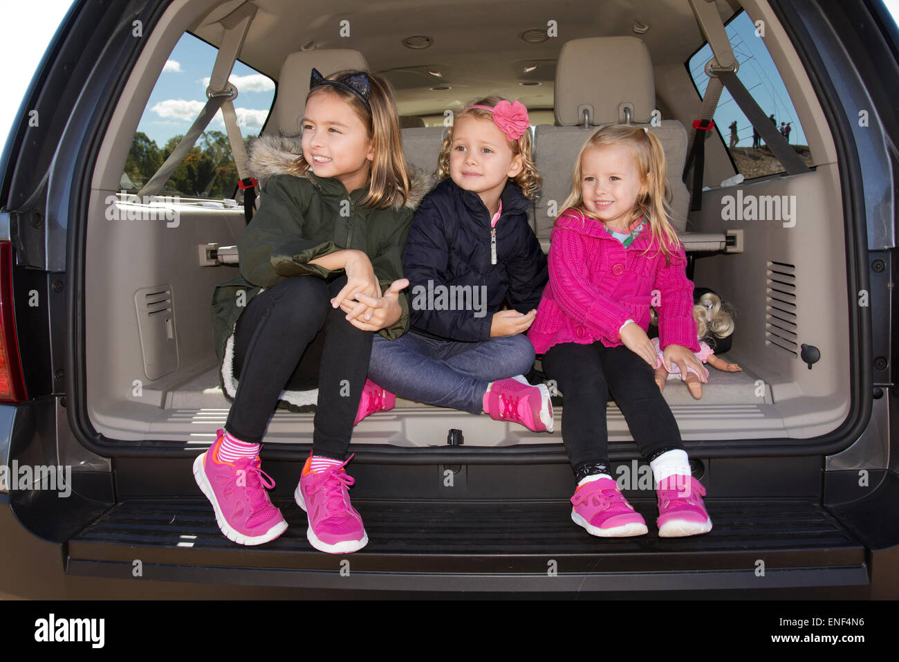 Tre giovani ragazze con lo stesso colore e stile di scarpe seduto nel bagagliaio di una vettura Foto Stock