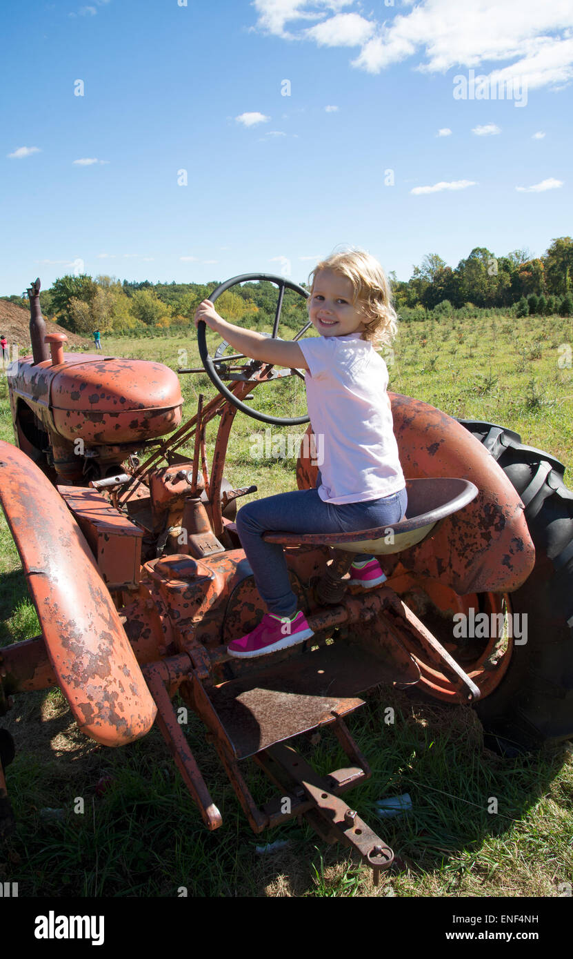 Bambina gioca su un vecchio rosso ruggine trattore agricolo bambino la sterzatura di un veicolo Foto Stock