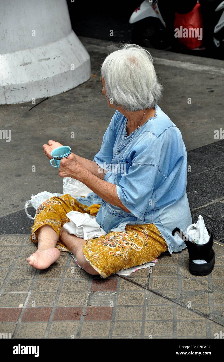 Bangkok, Thaiand: Un anziana donna disabile seduto sul marciapiede per l'accattonaggio denaro sulla Silom Road Foto Stock