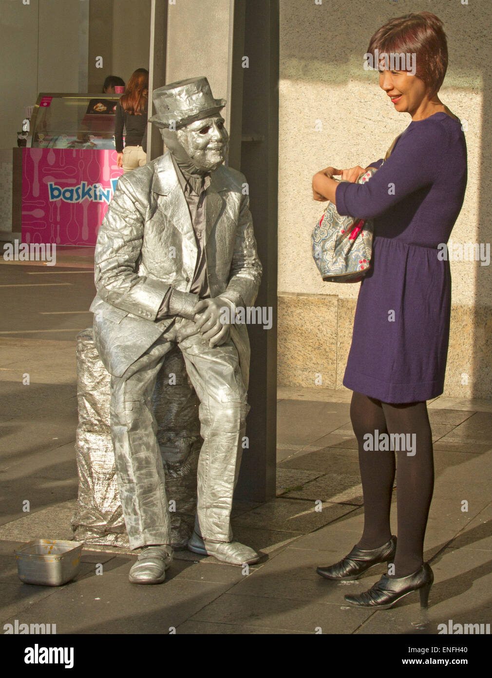 L'uomo musicista di strada come statua vivente con corpo argento, vestiti e hat interagenti con sorridente donna asiatica al Circular Quay di Sydney Australia Foto Stock