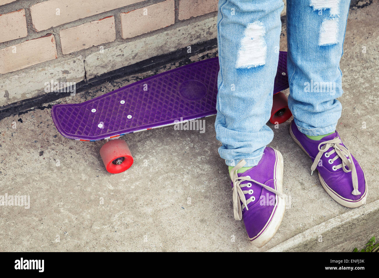 Adolescente in blue jeans e gumshoes stand con lo skateboard vicino grigio parete urbana, frammento di piedi Foto Stock