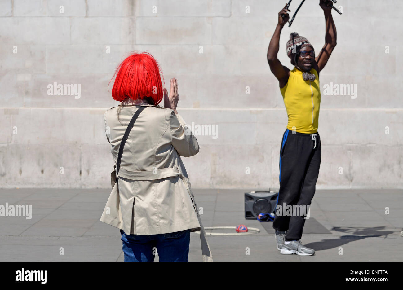 Londra, Inghilterra, Regno Unito. Donna con luminosi capelli rossi guardando un esecutore di strada in Trafalgar Square Foto Stock