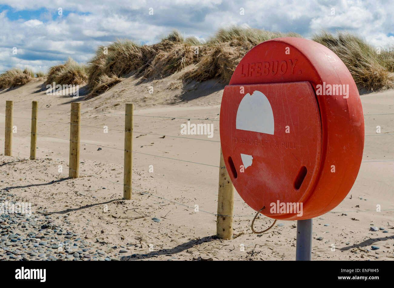 Un lifebouy titolare su un di sabbia e di ghiaia disseminata spiaggia con dune di sabbia in background Foto Stock