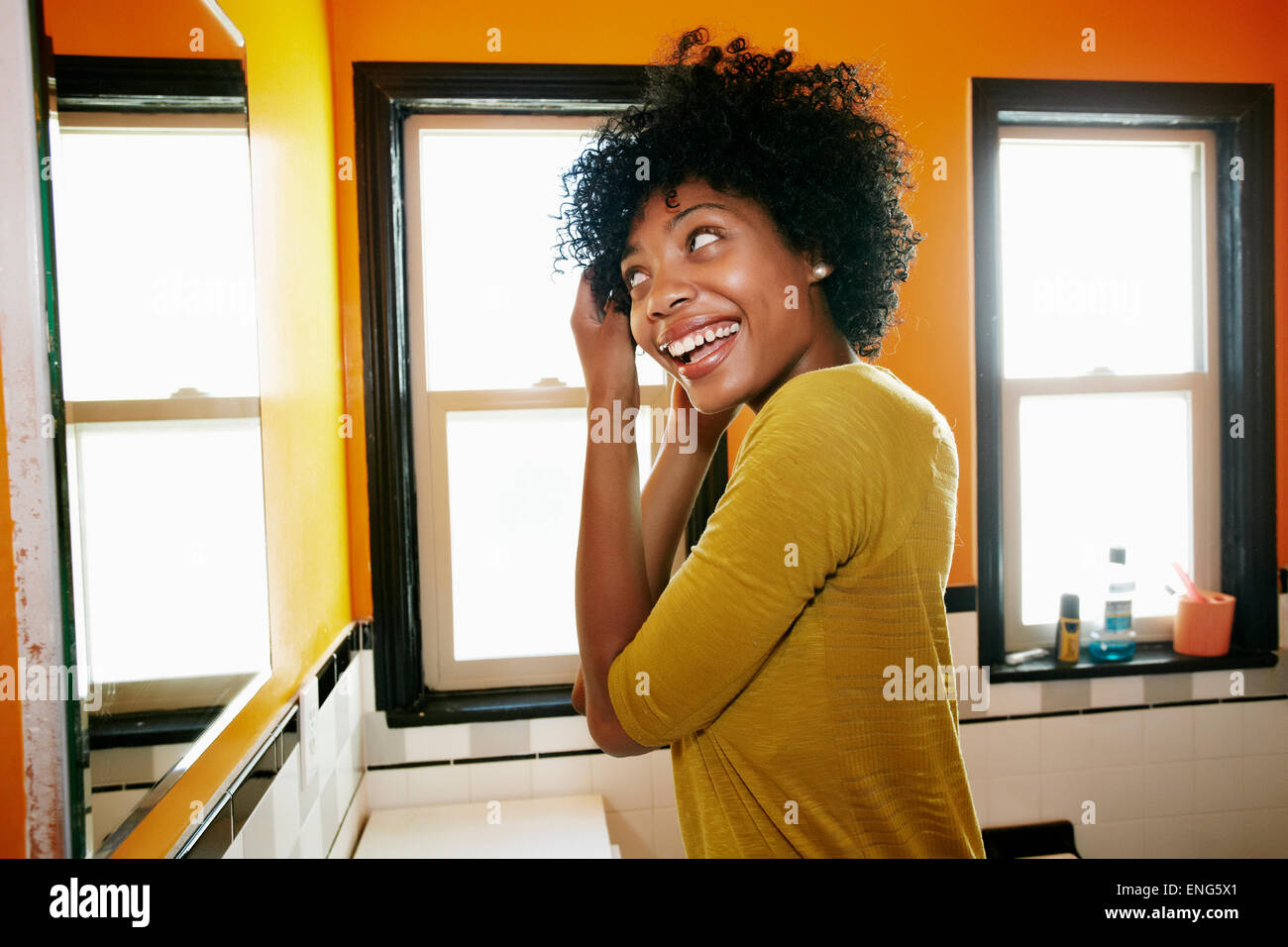 Sorridente donna nera per lo styling dei capelli nello specchio del bagno Foto Stock