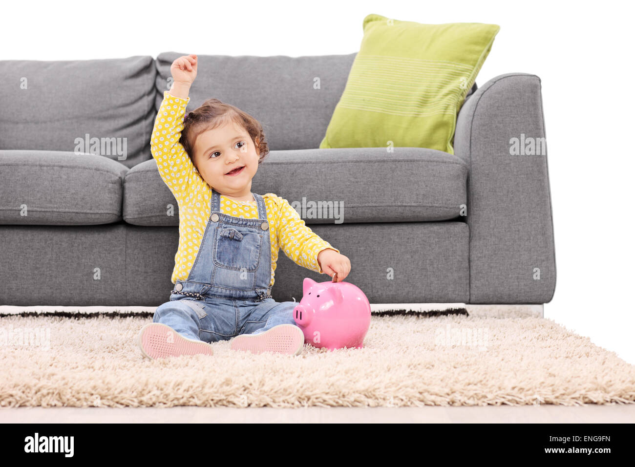 Studio shot di un simpatico bambina mettere soldi in un piggybank seduto sul pavimento nella parte anteriore di un moderno edificio grigio divano Foto Stock