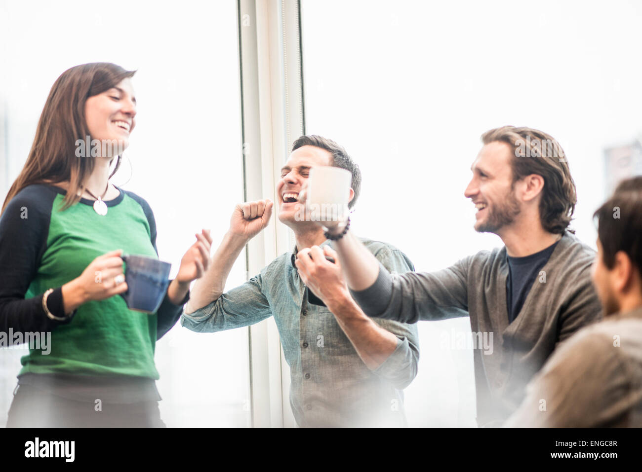 Quattro colleghi di lavoro su una pausa, ridendo e sollevando la loro tazze da caffè. Foto Stock