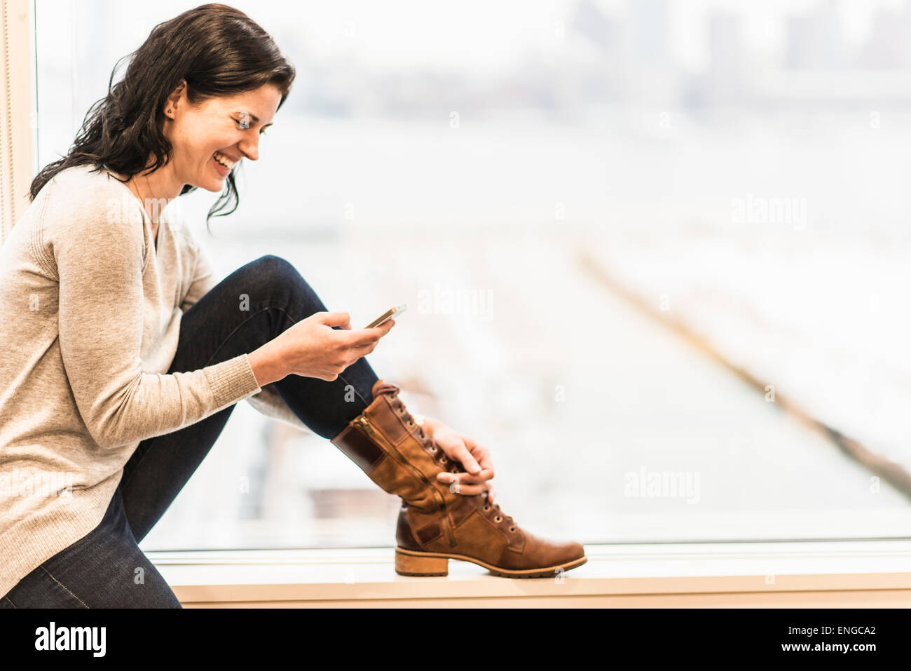 Un business donna seduta da una finestra utilizzando il suo smart phone. Foto Stock