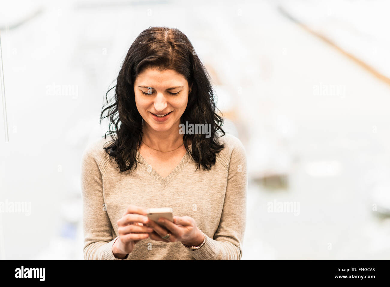 Un business donna seduta da una finestra utilizzando il suo smart phone. Foto Stock