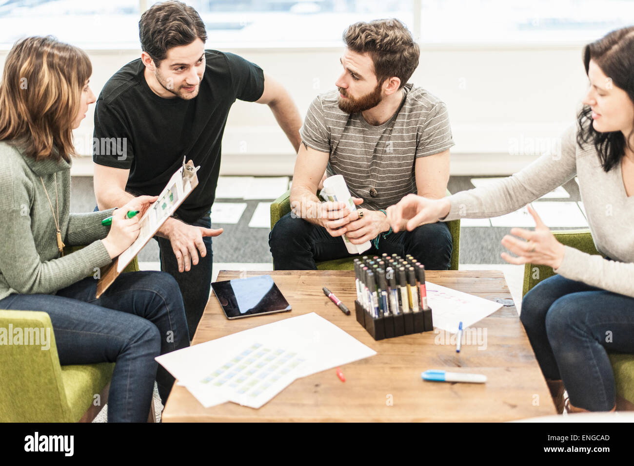 Quattro persone sedute a un tavolo i colleghi ad una riunione di pianificazione azienda penne colorate e lavoro su carta e compresse. Foto Stock