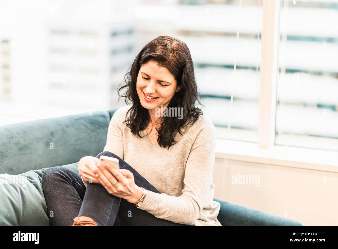 Una donna seduta con i suoi piedi su un divano, guardando il suo smart phone. Foto Stock