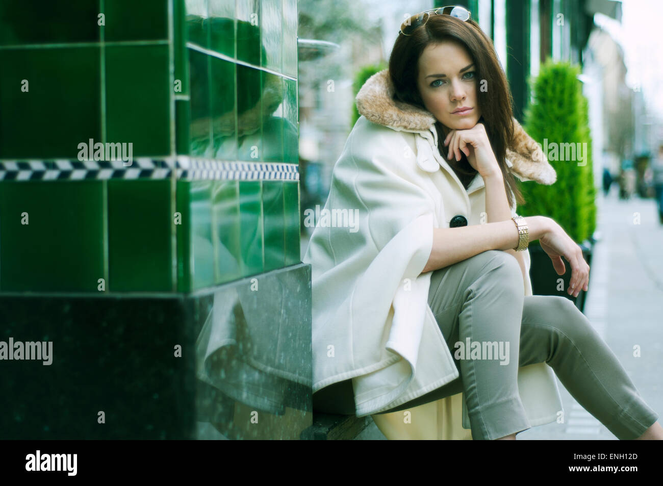 Giovane donna in una crema da spalmare sat al di fuori di un verde edificio piastrellato su una tranquilla strada di Londra Foto Stock