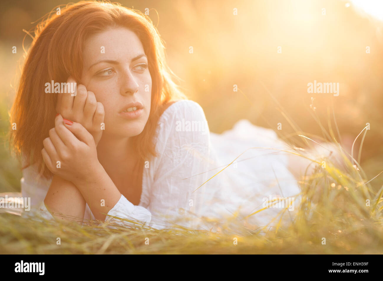 Giovane donna con capelli auburn posa in un campo illuminate dal sole al tramonto Foto Stock