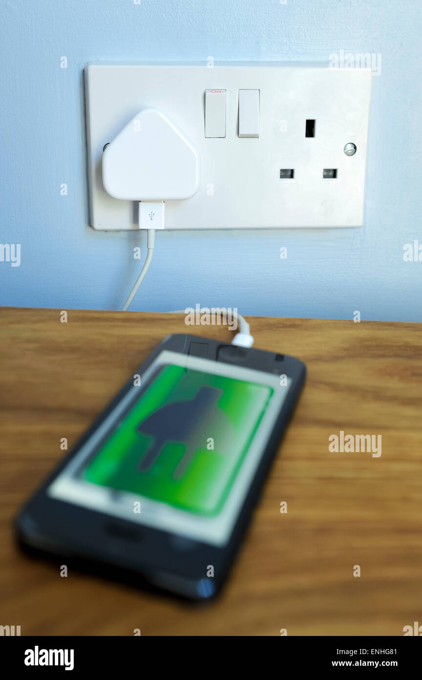 Iphone 5 mobile phone su carica in una spina UK socket. Foto Stock