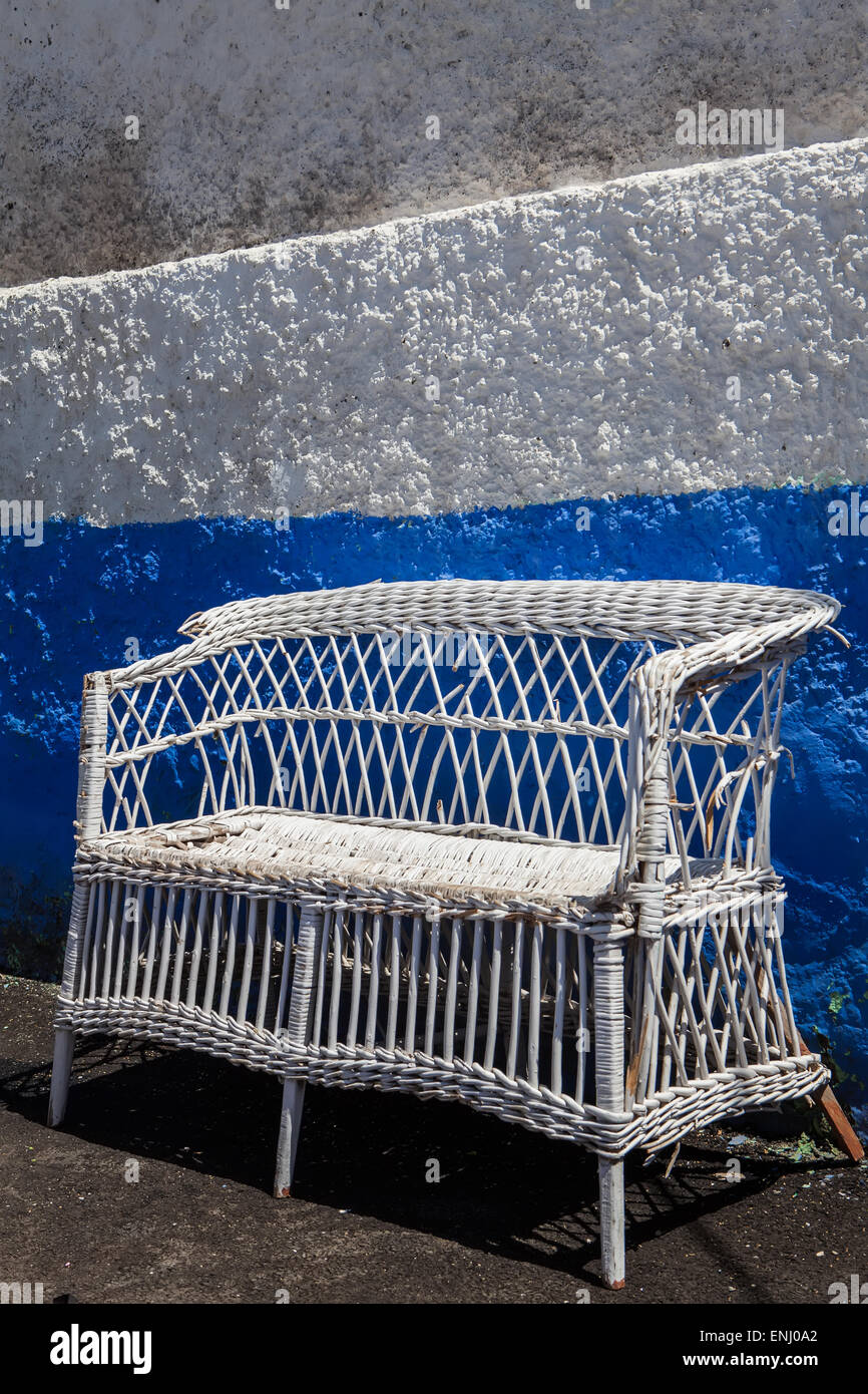 Vecchia sedia di vimini sul colore bianco nella parete blu Foto Stock