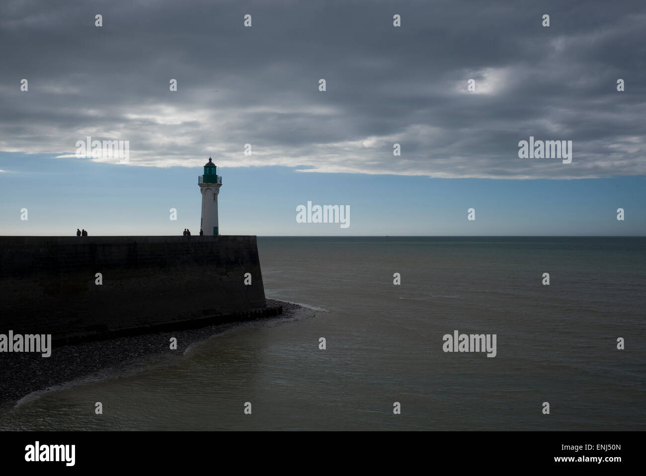 Faro e parete del porto, mare calmo, nubi minacciose, persone in silhouette Foto Stock