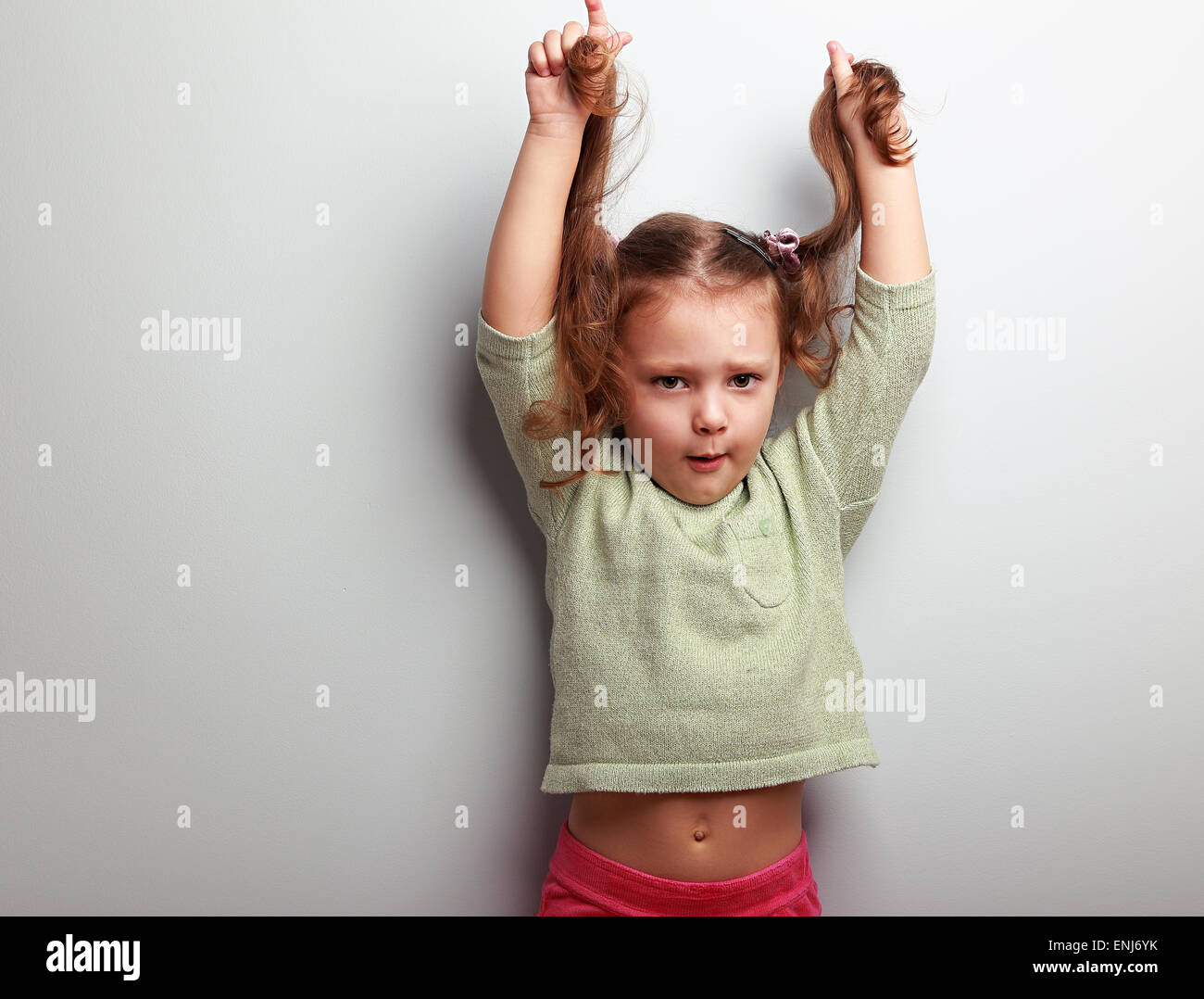 Active infelice ragazzo ragazza tirando i suoi lunghi capelli sulla parete blu con sfondo vuoto lo spazio di copia Foto Stock