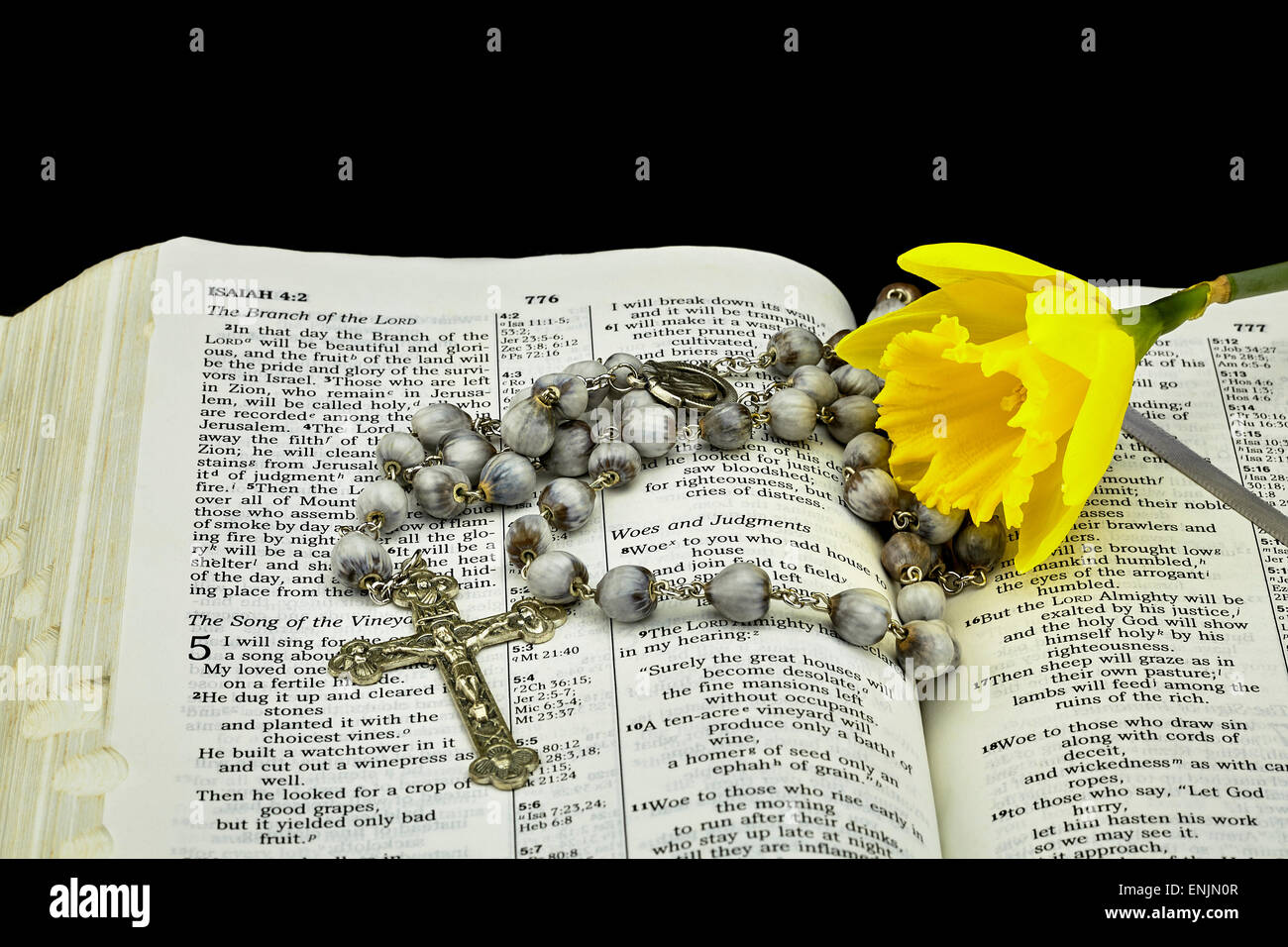 Primo piano di un'annata di posti di lavoro le lacrime cordone rosario e il crocifisso con un daffodil fiore su una Bibbia aperta a Isiah su sfondo nero Foto Stock