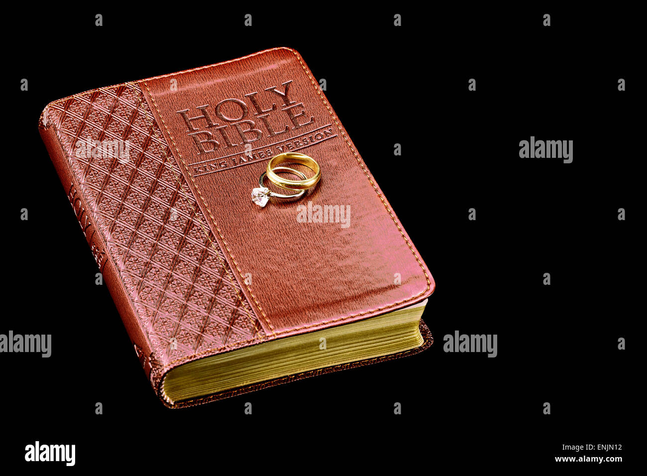 La Santa Bibbia con gli anelli di nozze isolato su nero Foto Stock