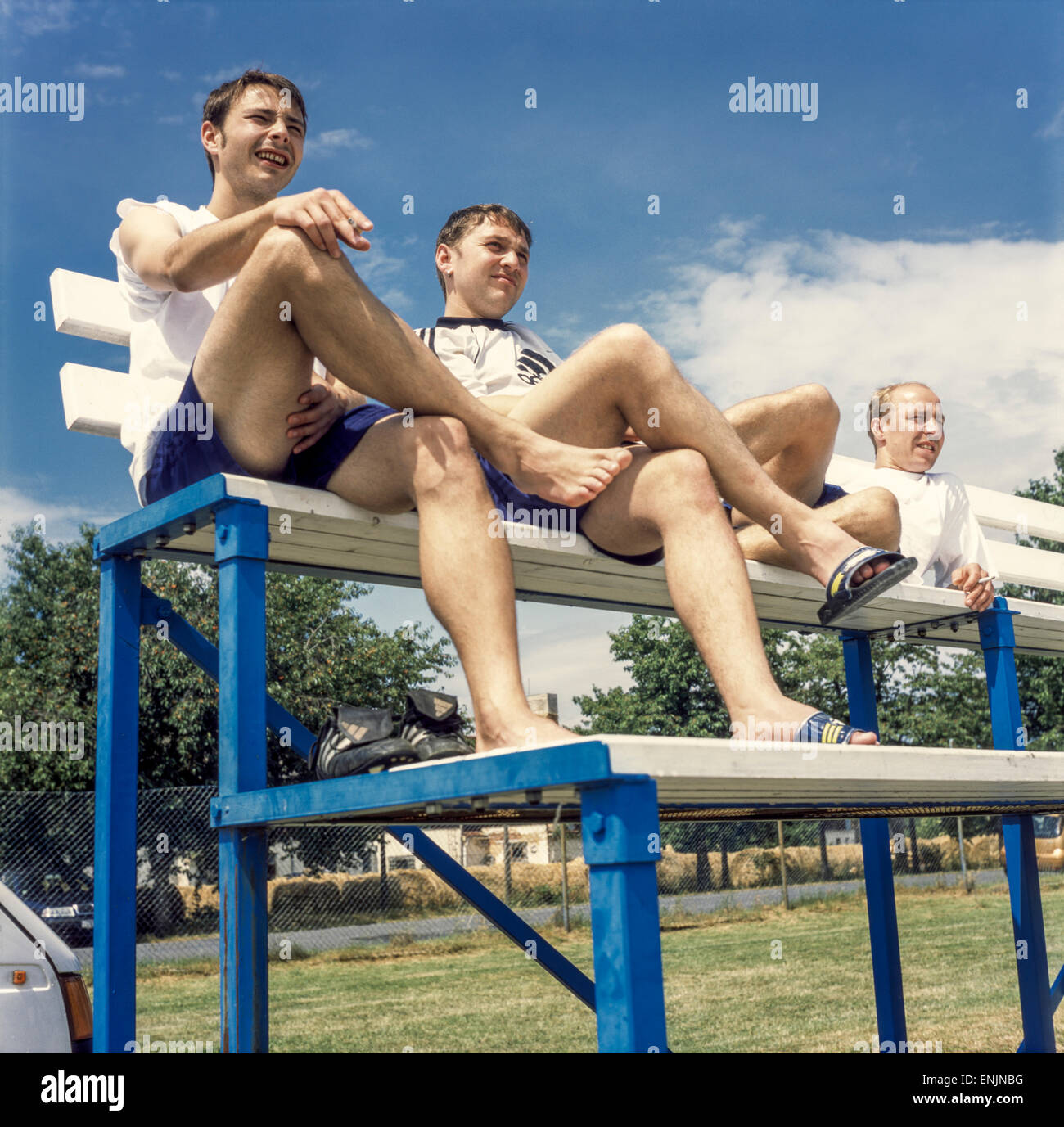 Tre giovani uomini europei su una panchina che guardano una partita di calcio rurale, Repubblica Ceca Foto Stock