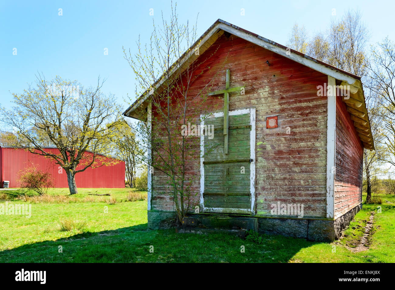 Piccolo rosso e weathered casa senza finestre. Chiuso la porta verde e una croce di legno su di esso. Rosso moderno edificio in metallo in backgr Foto Stock